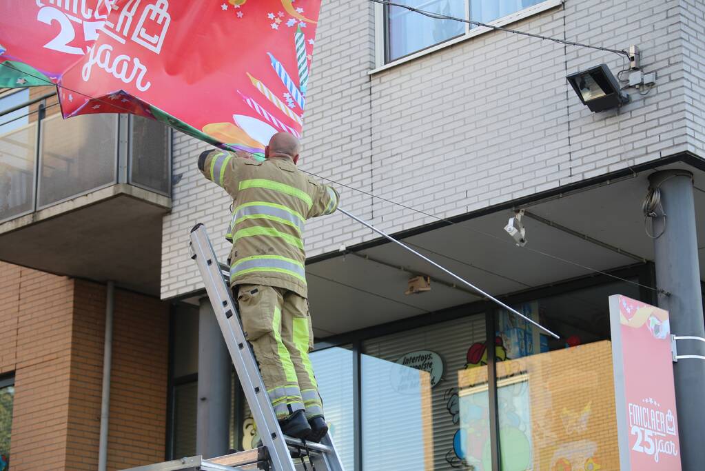 Brandweer zet loshangend reclamedoek vast