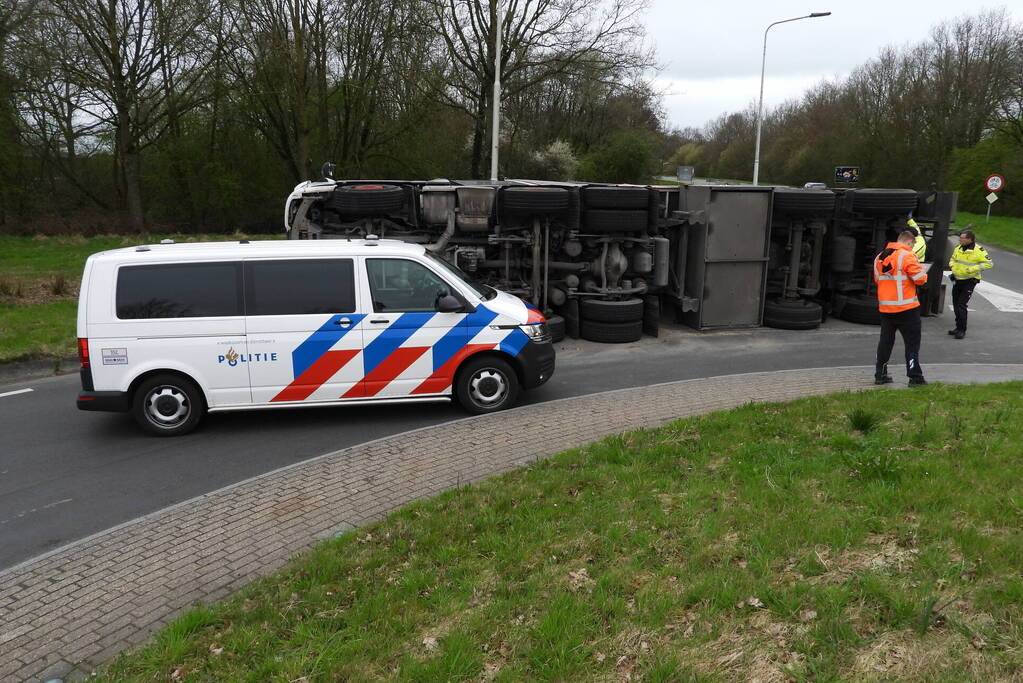 Vrachtwagencombinatie met zand kantelt op rotonde