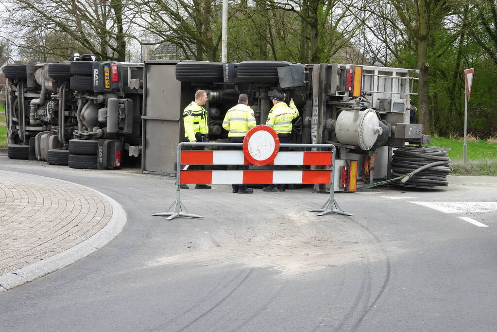 Vrachtwagencombinatie met zand kantelt op rotonde