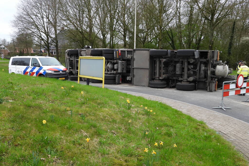 Vrachtwagencombinatie met zand kantelt op rotonde