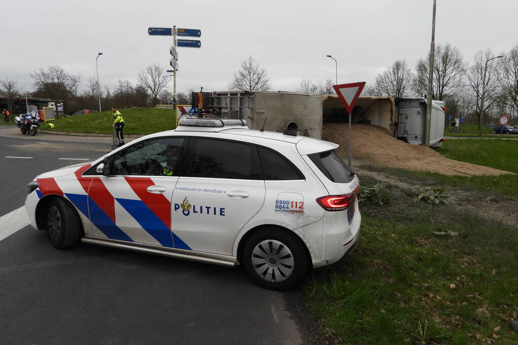 Vrachtwagencombinatie met zand kantelt op rotonde