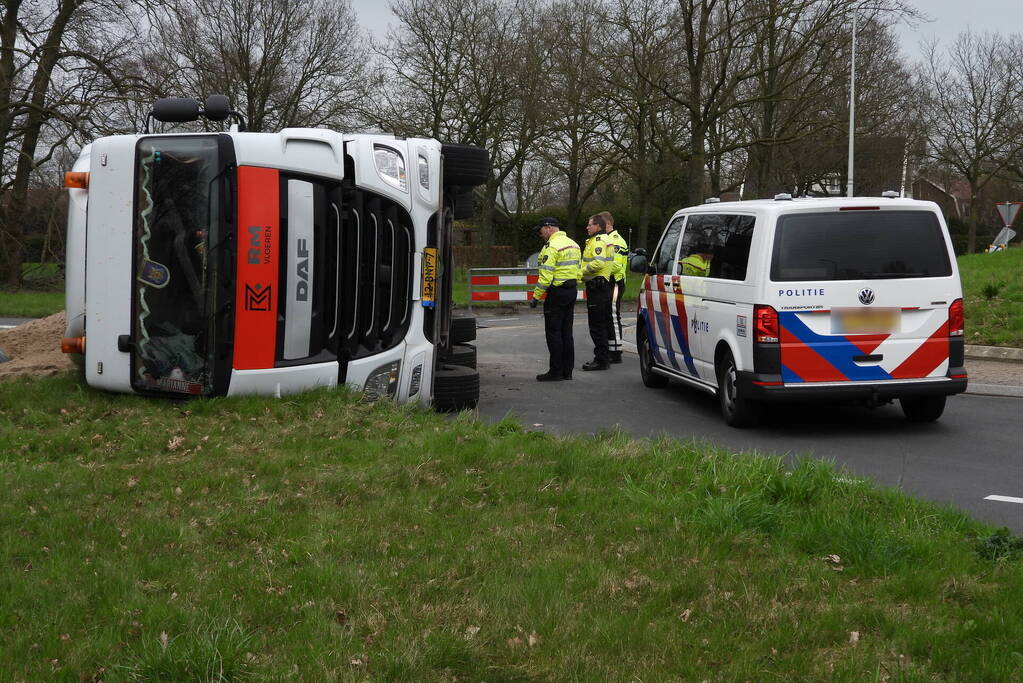 Vrachtwagencombinatie met zand kantelt op rotonde