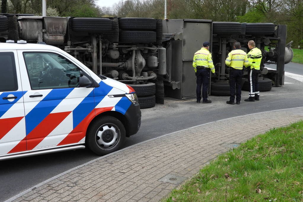 Vrachtwagencombinatie met zand kantelt op rotonde