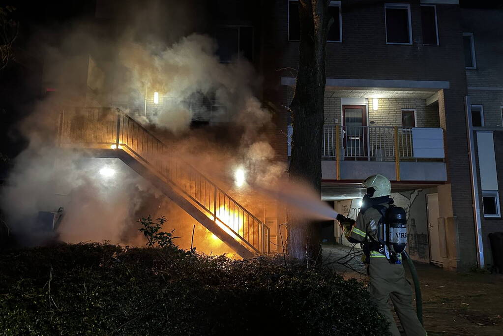 Brandweer blust brandende container onder trap