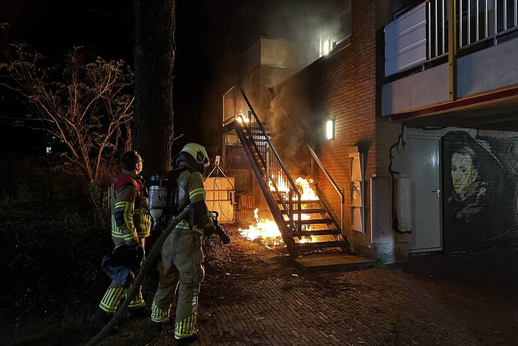 Brandweer blust brandende container onder trap