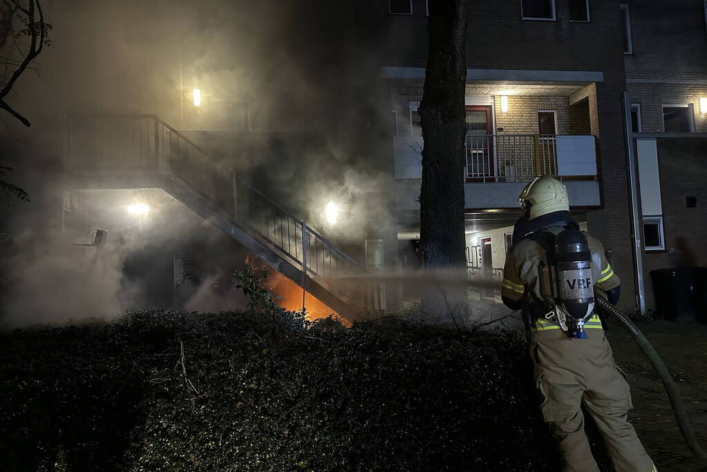 Brandweer blust brandende container onder trap