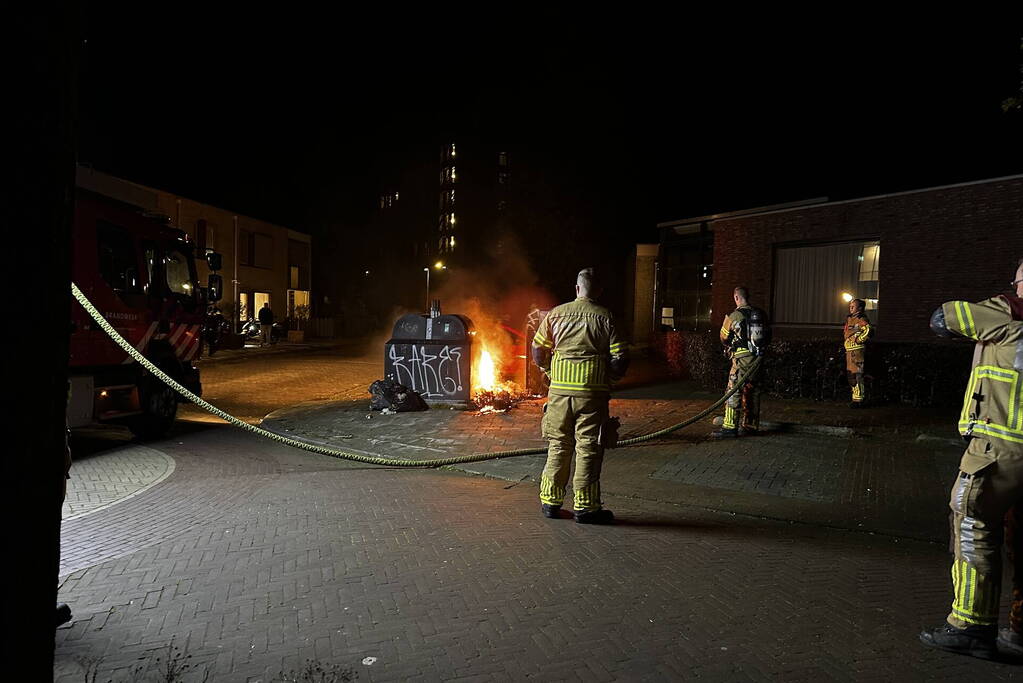 Brandweer blust brandend afval naast container