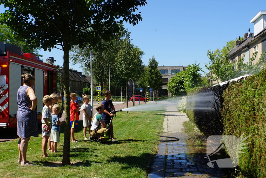 Kinderen blussen met brandweer brandende coniferenhaag