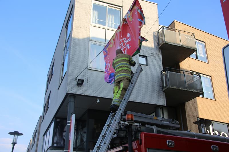 Brandweer zet loshangend reclamedoek vast