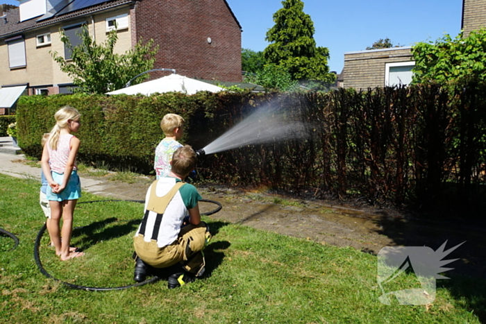 Kinderen blussen met brandweer brandende coniferenhaag